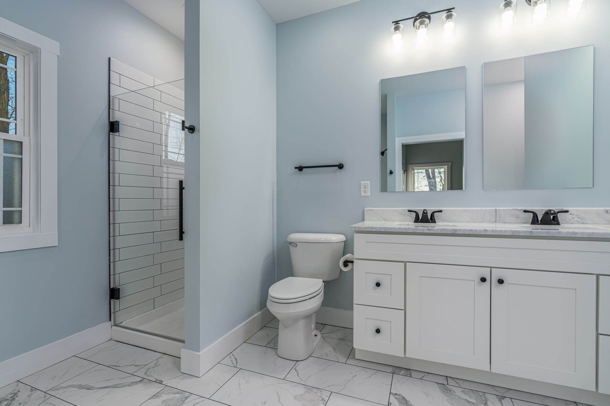 Farmhouse style bathroom with white cabinets, granite countertops, a subway tile shower, and blue walls.