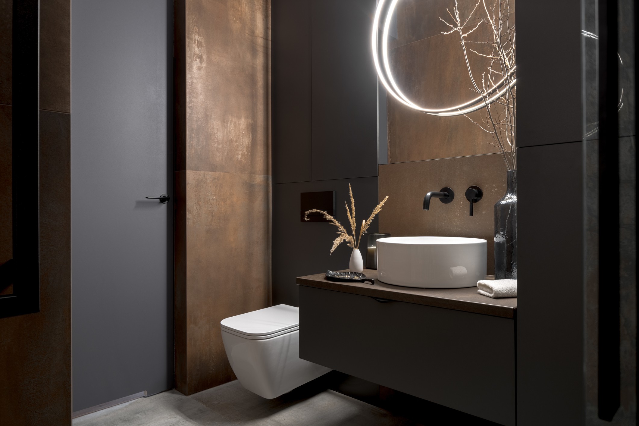 Dark, modern bathroom with rusty-toned wall tiles, and black and white fixtures.
