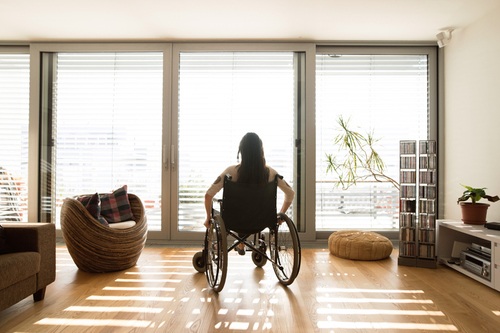 Woman With a Motor Disability Looking Through a Window in a Remodeled Living Room
